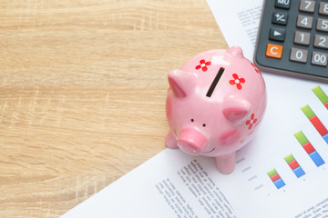 Pink piggy bank with graph and calculator on wooden desk - growing interest rate concept