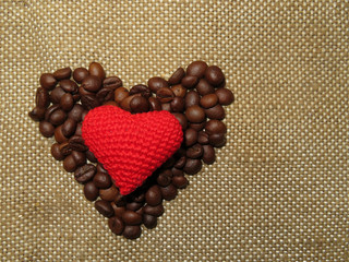 Coffee love: heart shape made of coffee beans with red knitted heart on burlap