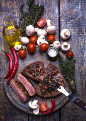 Grill Beef Steak, salt, pepper, garlic, rosemary, tomatoes, mushroom, olive oil  on the dark wooden board, background.