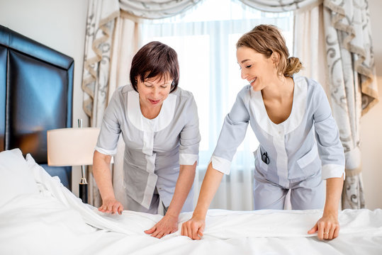 Two chambermaids in uniform making a bed with clean bedclothes in the luxury hotel bedroom
