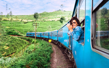Happy smiling woman looks out from window traveling by train on most picturesque train road in Sri Lanka - obrazy, fototapety, plakaty
