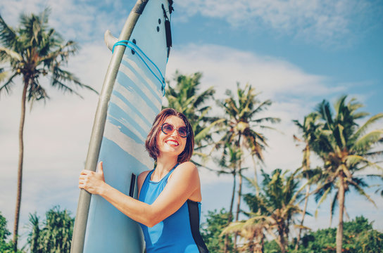 Happy smiling woman with surf board posing on tropical beach