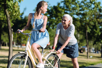 Obraz premium Go forward. Joyful happy nice woman pushing a bike and smiling while helping her granddaughter