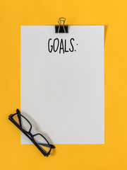 Top view goals list with notebook, glasses on yellow background with blank space for text. Flat...