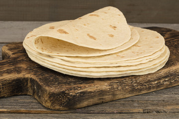 Board with stack of yummy tortillas on wooden table. 