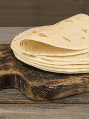 Board with stack of yummy tortillas on wooden table. 