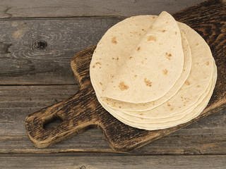 Board with stack of yummy tortillas on wooden table. 