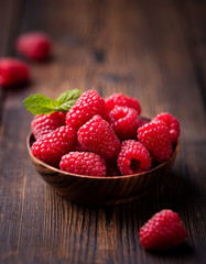 Ripe sweet raspberries in bowl on wooden table.