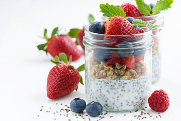Breakfast in a jar, chia with berries and oat flakes on white table, closeup