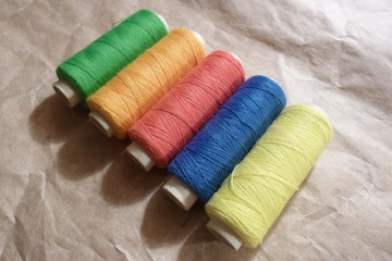  threads multicolored coil wound on coils with thread yarn natural material pastel color green pink yellow red brown blue orange close-up crumpled paper background for design backyard sewing accessori
