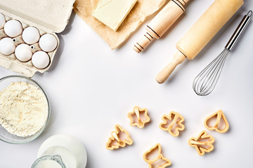 Objects and ingredients for baking, plastic molds for cookies on a white background. Flour, eggs, rolling pin, whisk, milk, butter, cream. Top view, space for text