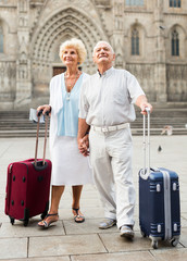 Senior woman and man travelling together, walking with baggage on city