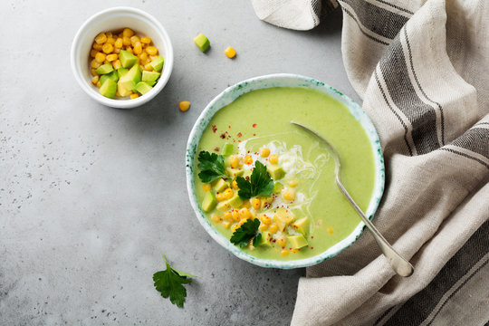 Homemade tender soup puree from avocado and corn with cream in rustic ceramic plate on gray concrete old background. Selective focus. Top view. Copy space.