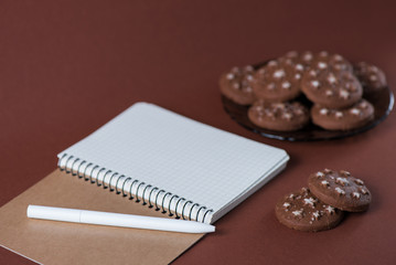 Top view of a notebook with a pen in a chocolate biscuit on a pink background
