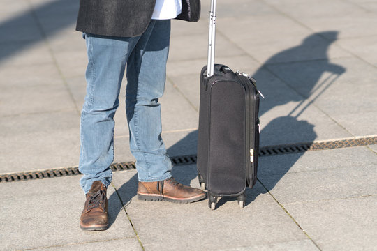 Cropped image of male legs and black trolley suitcase. Outdoors