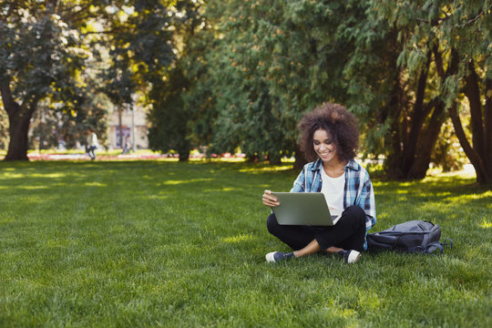Cheerful young woman using laptop in park