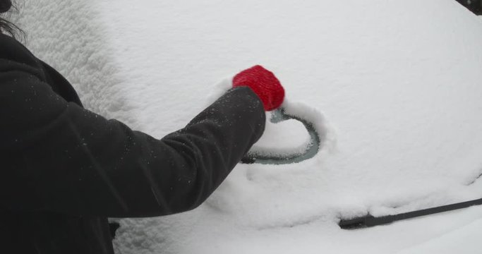 A woman is refining an afore drawn heart shape on the windscreen of a snow-covered car - ProRes
