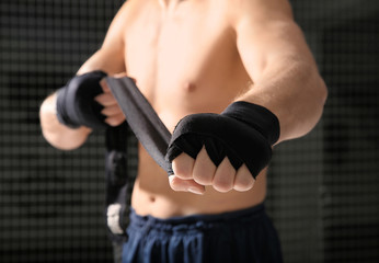 Fototapeta premium Young boxer applying wrist wraps in gym, closeup