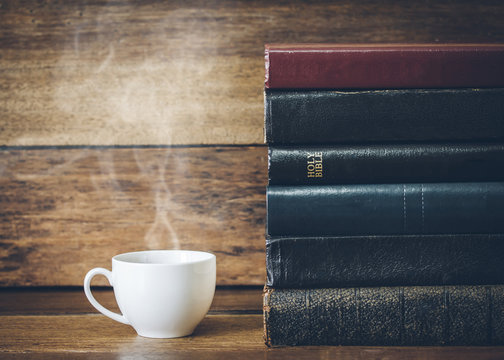 a cup of coffee and  stack of book with  holy bible on wooden background
