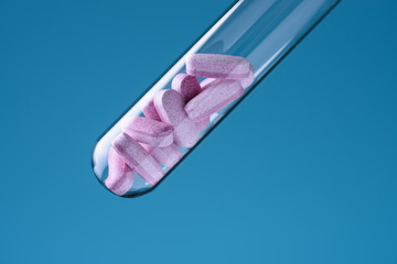 Laboratory glass test tube filled with pink pills on blue backround. Medicine research concept.
