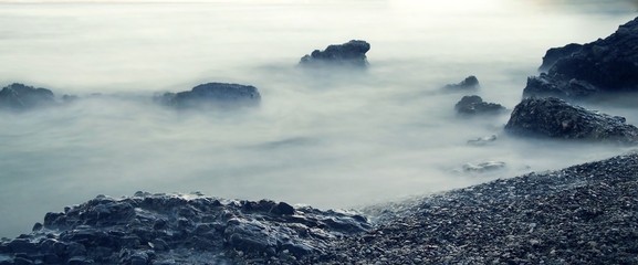 Panoramic seascape. Water rolling over rocks at coastline mist long exposure scenic background