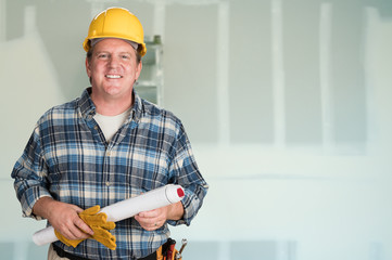 Contractor with Plans and Hard Hat In Front of Drywall.