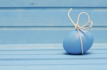 
Blue Easter egg with white bow on blue wooden background 