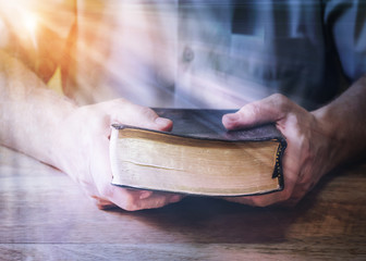 a man holding holy bible on wooden table with window light Bokeh effected