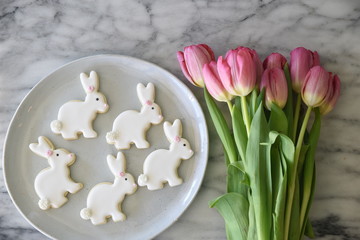 Iced, rabbit shaped cookies, on white plate, with pink tulips, overhead view