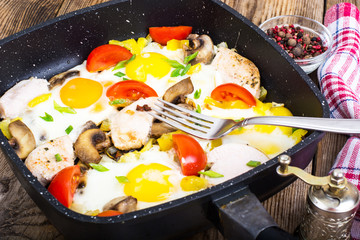 Fried eggs, tomatoes, ham, mushrooms in frying pan