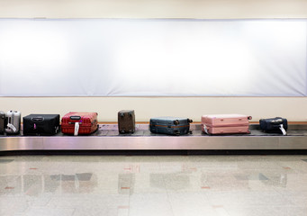 Many luggages are laying down on the conveyor belt at the airport.