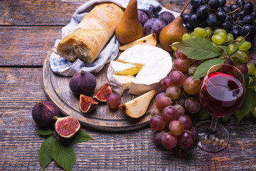 Red wine in the glass, cork, bottle screw and a set of products - cheese, grapes, nuts, olives, peas, figs on a wooden board, background