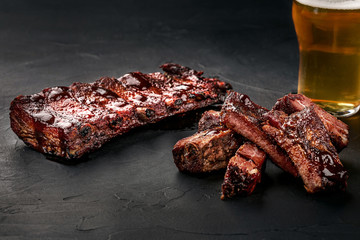 Pork ribs in barbecue sauce and a glass of beer on a black slate dish. A great snack to beer on a...