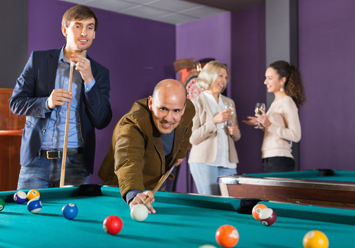 Group of cheerful friends playing billiards