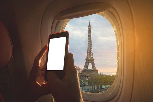 Woman sitting by aircraft window and using a digital mobile during the flight. Eiffel tower as seen through window of an aircraft. - Powered by Adobe