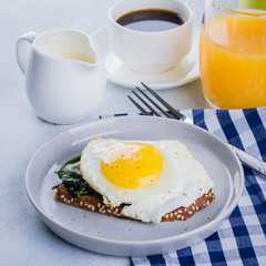 Fototapeta premium Rye bread toasts with fried spinach and egg with cup of coffee and orange juice on blue table background. Healthy Breakfast Food Concept.