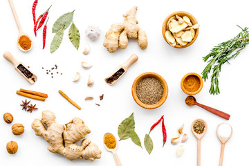 Colorful dry spices in bowls and spoons near ginger, garlic, rosemary on white background top view