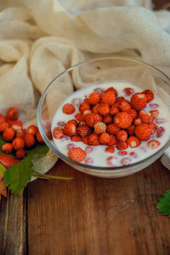 Fresh milk yoghurt with wild strawberries and granola served in a glass jar with mint leaves on white wooden table with striped red napkin. Healthy summer breakfast concept. Top view.