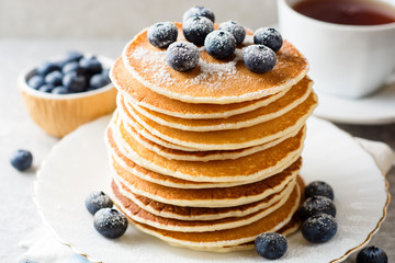 Pancakes with blueberries and sugar on grey stone background.