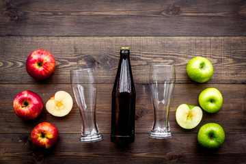 Apple cider. Low-alcoholic beveradge in dark bottle near beer glasses and fresh apples on dark wooden background top view copy space