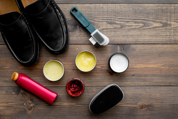 Shoe polish, brushes, wax near black shiny leather shoes on dark wooden background top view copy space