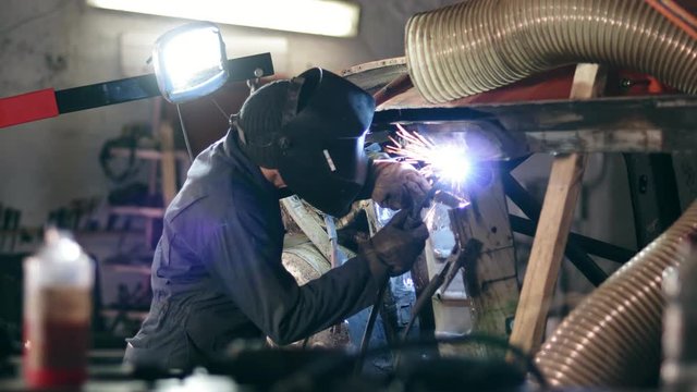Male worker at a welding factory in a welding mask is working with metal construction. Welding on an industrial plant. Slow motion.
