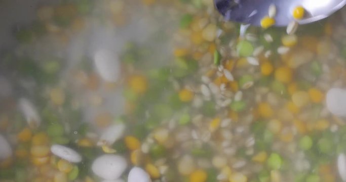 Using a spoon to stir vegetable soup mix in water while cooking.