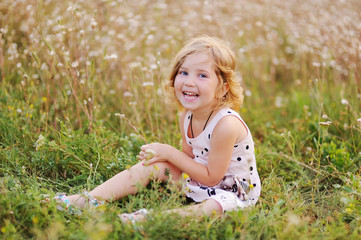 Naklejka na ściany i meble baby girl sitting in the grass on a background of flowers and smiling at the camera