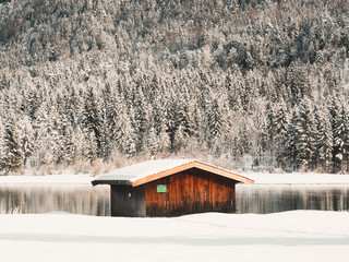 Bootshaus bei winterlichem Bergsee im Sonnenschein