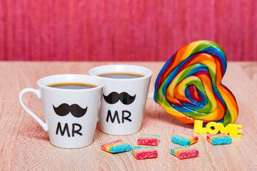 Gay marriage concept. Two cups of coffee, rainbow lollipop heart and candy
