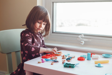 Portrait of cute white Caucasian preschooler girl playing plasticine playdough indoors at home. Early creativity brain development concept. Children activity. Fine motor skills.