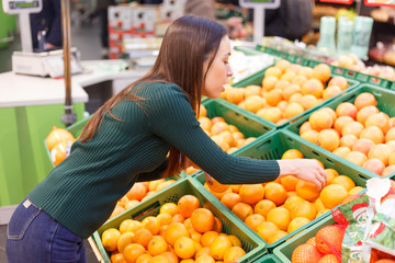 A young woman in a store chooses oranges.