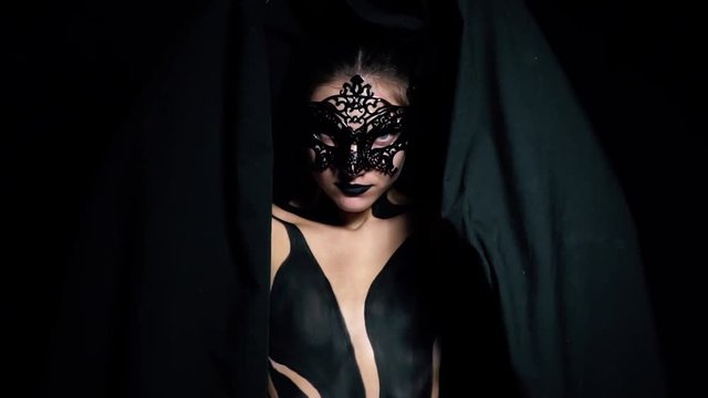Slow motion shooting a girl in a mask and black body art closes herself with a cloth