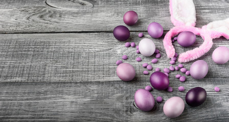 Easter eggs in a fashionable coloring on a gray wooden background with a female hoop with Easter bunny ears